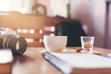 A cup of coffee on a table with a notebook and camera in a cafe
