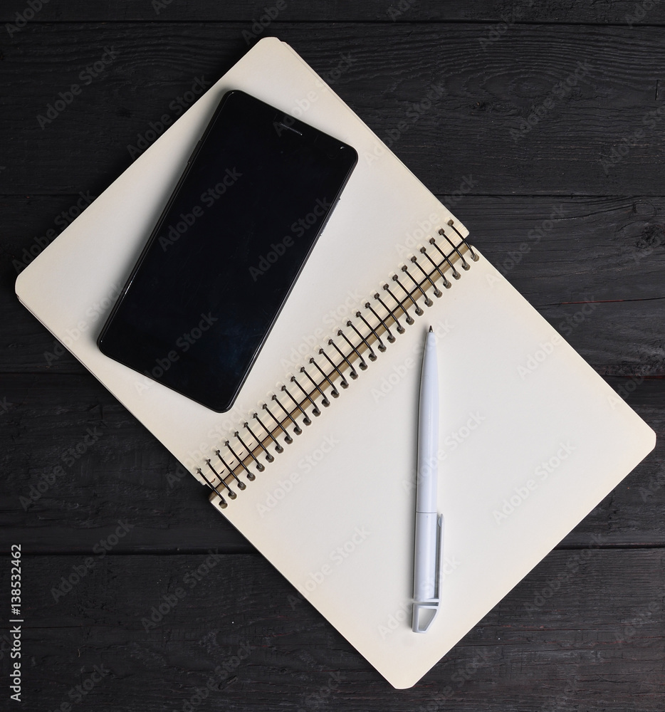 Poster notebook with a pen and smartphone on a black wooden table. working space.