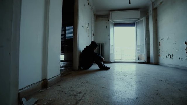 Hooded depressed young man in empty abandoned house