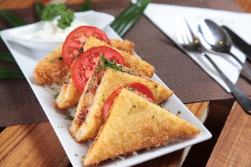 portion fried sandwich with bread crumb, triangle cut on restaurant table with sliced tomato