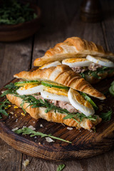 Tuna salad sandwich with boiled egg, arugula, cucumber and tuna salad on wooden cutting board. Closeup view, selective focus