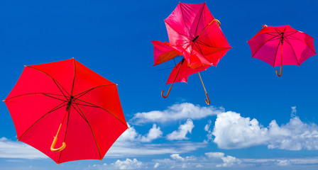 parasols rouges chahutés et emportés par le vent, fond ciel bleu 