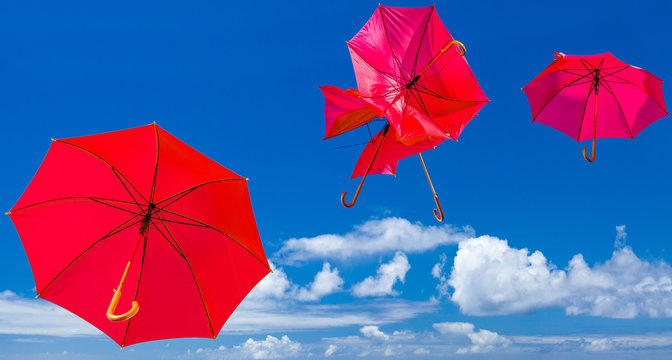 parasols rouges chahutés et emportés par le vent, fond ciel bleu 