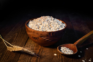oat flakes in a wooden bowl on a wooden background near the ears of wheat. Wooden spoon with flakes