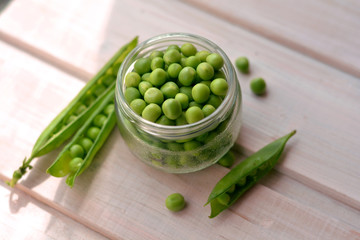 Top view of fresh, sweet pea seeds in glass plate near green, split pea pods on wooden background