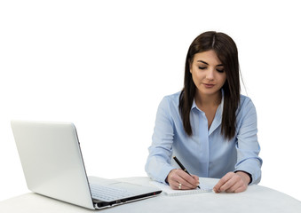 Young girl sitting in the office with a laptop and is writing in a notebook. White isolated background.