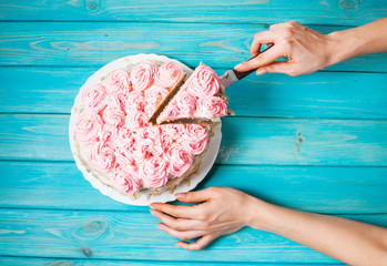 Woman's hands cut the cake with pink cream on blue wood background. Pink cake.