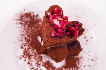 Heart shaped slices of a brownie decorated with pomegranate on white background