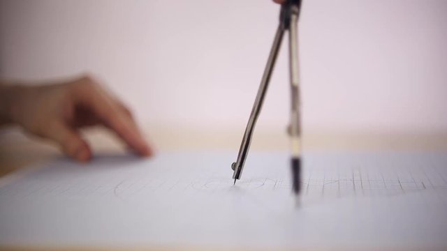 Draftsman uses the compass on a sheet of paper, she draws a circle, close-up
