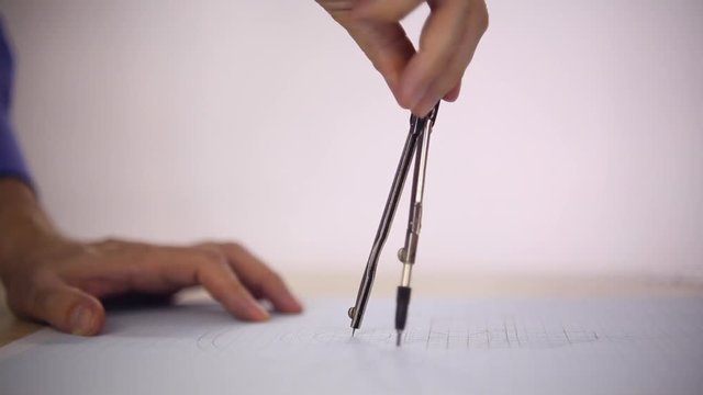 Draftsman uses the compass on a sheet of paper, he draws a circle, close-up

