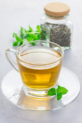 Herbal mint tea in a glass cup with dry peppermint tea on background, vertical