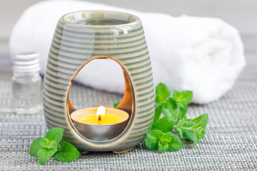 Peppermint essential oil in aroma lamp on gray mat with spa background, horizontal