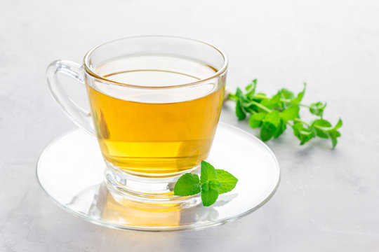 Herbal mint tea in a glass cup with fresh peppermint on background, horizontal