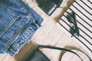 perfect spring outfit accessories. flat lay of a trendy fashion outfit, denim jeans, striped shirt, black ankle boots and a small elegant black purse. top view.

