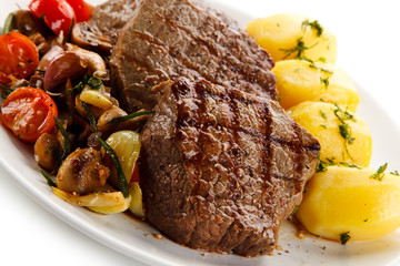 Grilled steaks, boiled potatoes and vegetable salad on white background 