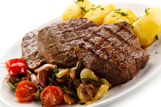 Grilled steaks, boiled potatoes and vegetable salad on white background 