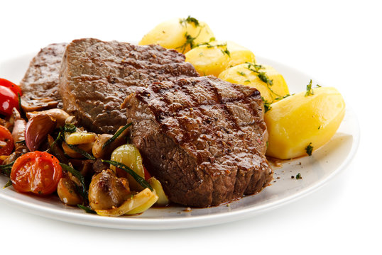 Grilled steaks, boiled potatoes and vegetable salad on white background 