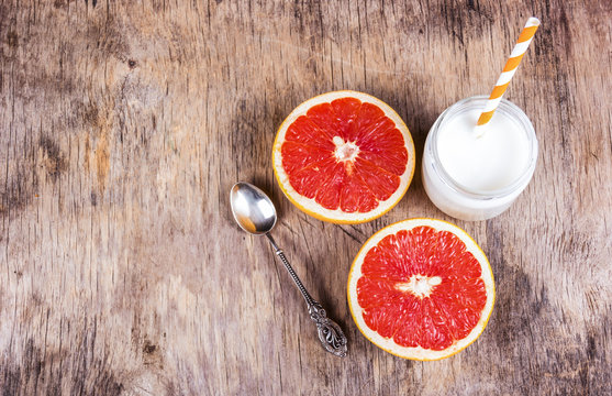 Two halves of juicy grapefruit, vintage silver spoon and homemade yogurt on the old wooden background. Copy space.