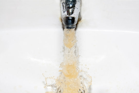 Dirty Brown Running Water Falling Into A White Sink From Tap