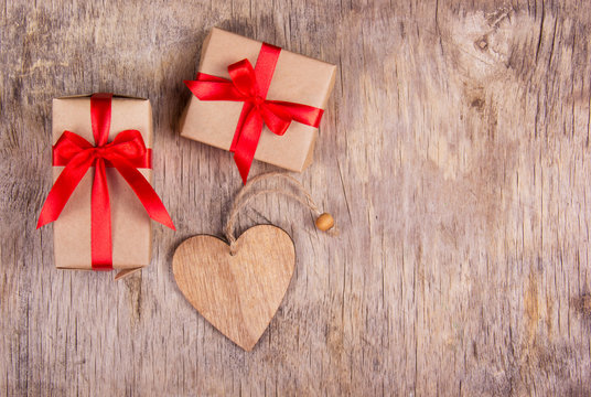 Gift box with a red bow and wooden heart on an old wooden table. Copy space.