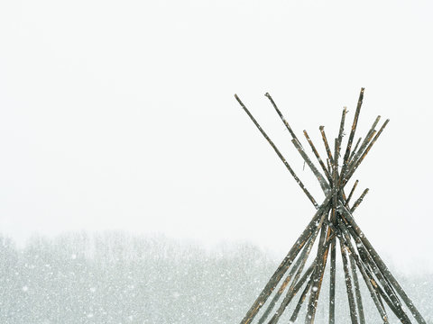 House of tree trunks drawn up cone (Tent Scaffolds) in winter. Wigwam, tent, teepee, yurt, kibitka in inclement weather, snowstorm, snowfall.