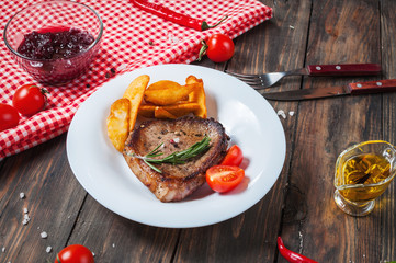 Grilled beef steak seasoned with spices served on a wooden board with fresh cherry tomato, baked potatoes and red hot chili peppers