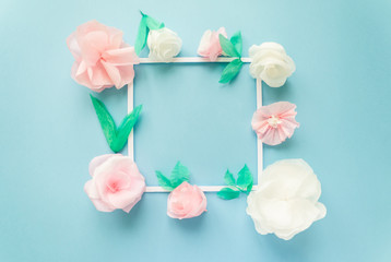 square frame with color paper flowers on the blue background. Flat lay. Nature concept
