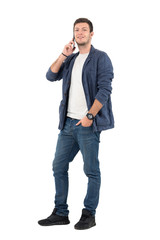 Fototapeta premium Happy smiling man in jeans and denim shirt talking on the phone looking at camera. Full body length portrait isolated over white background.