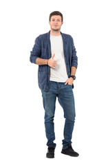 Happy young man in rolled up sleeves in denim shirt with thumbs up gesture. Full body length...