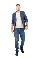 Young confident man in denim unbuttoned shirt and jeans walking towards camera. Full body length portrait isolated over white background.