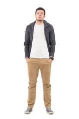 Casual man wearing zip sweater over white shirt posing with hands in pockets. Full body length portrait isolated over white background.