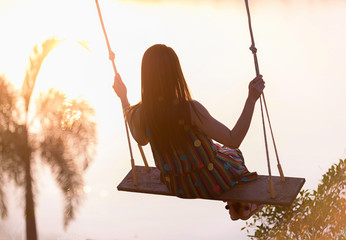 silhouette young woman on a swing with sunset background
