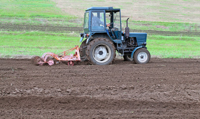 Tractor with cultivator harrow the ground fastened. Summer season opens plowing and cultivating the garden.