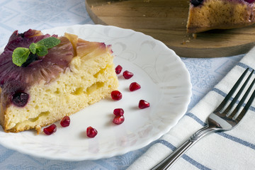 Homemade pineapple upside down cake with a slice of cake and pomegranate seeds on white plate with fork on light cloth napkin