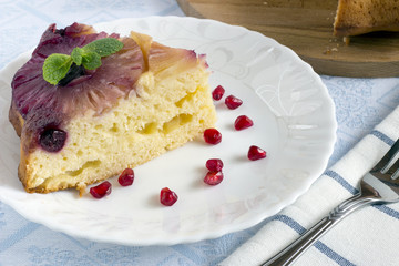 Homemade pineapple upside down cake with a slice of cake and pomegranate seeds on white plate with fork on light cloth napkin