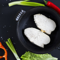 Baked white meat in iron pan with sea salt, red paprika, green onion, leafy green salad and cayenne pepper on black background