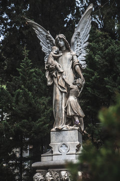 Sculpture of an angel on a cemetery with children against the background of leaves