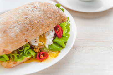 breakfast in a rustic style on a white wooden surface. ciabatta with poached egg and grain mustard with a hot cup of coffee and fresh