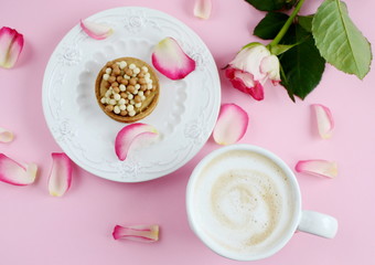 Cup of cappuccino and cake with pink roses on the table