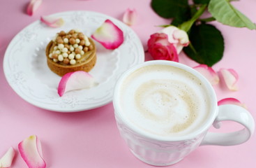 Cup of cappuccino and cake with pink roses on the table