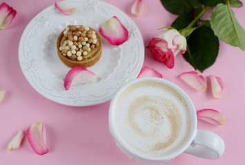 Cup of cappuccino and cake with pink roses on the table