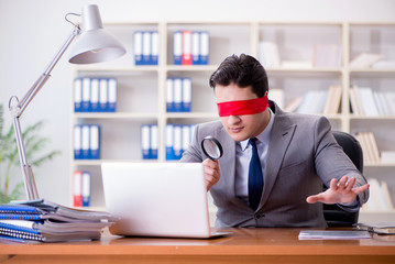 Blindfold businessman sitting at desk in office