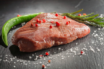raw beef steak with rosemary and peppers on dark stone