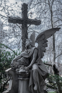 Sculpture of a sad angel on a cemetery against the background of leaves