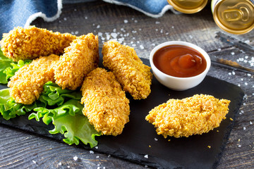 Hot, crispy chicken and fresh lettuce on a slate board. Snack fast food and beer on a wooden table.