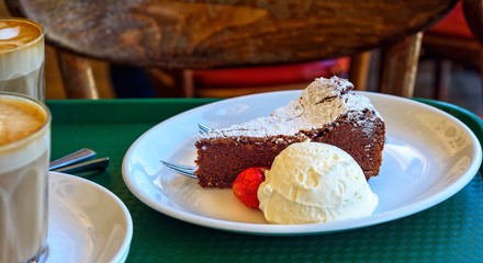 A slice of chocolate cake with creak, a strawberry and two cups of coffee on a green tray