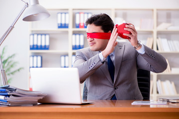 Blindfold businessman sitting at desk in office