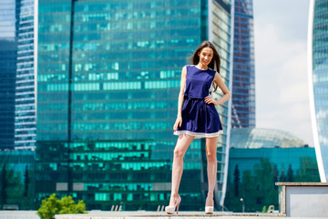 Young woman in a blue dress is stretching near skyscrapers