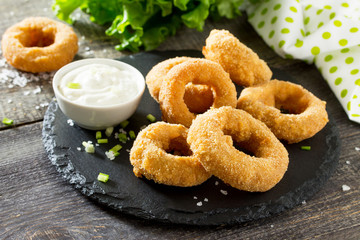Onion rings fried with cheese on slate board. Snack food to beer on a wooden table.