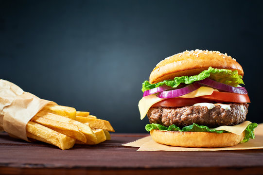 Craft beef burger and french fries on wooden table isolated on black background.